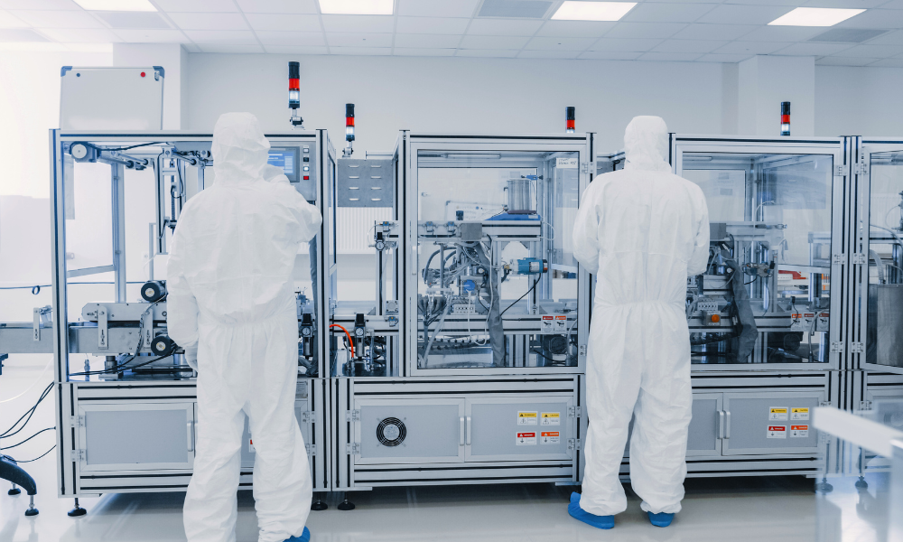 Two scientist are in complete PPE gear at they use equipment for aseptic manufacturing.